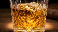 Golden whiskey with ice cubes in crystal cut glass tumbler on wooden surface, amber liquid alcohol beverage for luxury bar and restaurant service.