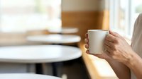 Mature adult holding ceramic mug with hot beverage in modern kitchen or dining space, morning routine, breakfast time, lifestyle and wellness concept.