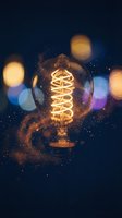Vintage Edison bulb with glowing filament surrounded by bokeh lights and sparkling particles on dark background, suitable for energy, innovation, and creativity concepts.