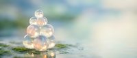 Transparent soap bubbles stacked in pyramid formation on mossy surface with soft bokeh background creating dreamy natural scene for wellness and relaxation concepts.