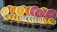 Fresh citrus slices arranged on rustic wood serving board - oranges, pink grapefruits and lemons creating colorful gradient display for entertaining and garnish.