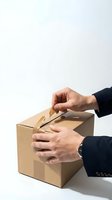 Man in dark business attire opening cardboard box with both hands against white background. Suitable for logistics, delivery, unboxing, e-commerce, shipping, and business concepts.