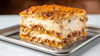 Traditional layered tiramisu dessert with mascarpone cream, coffee soaked ladyfingers and cocoa powder dusting served on metal plate, close up view of slice.