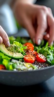 Fresh quinoa bowl with sliced avocado, cherry tomatoes and mixed greens garnished with black pepper. Close-up of hands preparing healthy lunch salad.