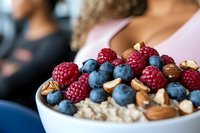 Fresh raspberries and blueberries with almonds on top of oatmeal in white ceramic bowl, healthy breakfast closeup with selective focus on berries.