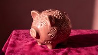 Decorative ceramic piggy bank with intricate floral patterns sits on luxurious velvet fabric, symbolizing savings and financial planning goals.