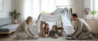 Happy family building blanket fort together in bright living room with parents and children creating cozy play space for bonding time at home.