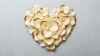 Heart shaped arrangement of white and gold flower petals on light gray background, luxury romantic decor for wedding or Valentine's Day.