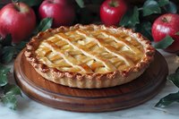 Homemade apple pie with lattice crust on wooden serving board, surrounded by fresh red apples and green leaves, traditional baking and dessert photography.
