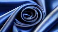 Elegant swirled navy blue silk fabric creates luxurious spiral pattern with soft folds and smooth texture, showcasing rich sheen and flowing movement for fashion design.