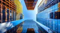 Looking up at modern glass skyscrapers from street level with dramatic perspective, blue sky and clouds reflecting in windows. Perfect for business, architecture and urban development themes.