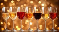 Wine glasses filled with different varieties from white to red arranged in row against warm bokeh background creating festive holiday atmosphere.
