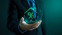 Businessman hand holding holographic house icon with percentage symbol and upward arrow chart for mortgage rates and real estate investment growth.