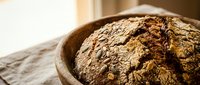 Freshly baked artisan bread loaf in rustic wooden bowl with crusty golden-brown exterior, ideal for bakery, food, and culinary content.