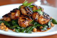 Grilled glazed chicken pieces with caramelized soy sauce served on sauteed fresh spinach and chickpeas, garnished with herbs on white plate. Restaurant quality meal.