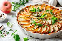 Homemade apple tart with fresh herbs in white ceramic dish on marble surface. Rustic autumn dessert with sliced fruit arranged in circular pattern.