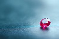 Brilliant pink ruby gemstone on shimmering turquoise surface with soft bokeh background creates elegant luxury jewelry mood for design and advertising.
