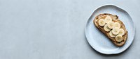 Toast topped with sliced banana on a white ceramic plate against a light gray textured surface, suitable for food blogs and healthy breakfast content.