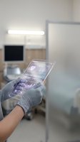 Medical professional using futuristic transparent tablet with holographic interface displaying health data and analytics in modern hospital setting.