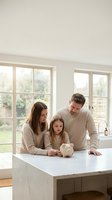 Happy Caucasian family with young daughter learning about savings with piggy bank in bright modern kitchen. Financial education and money management concept.