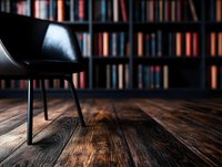Modern black chair against blurred bookshelf background with dramatic lighting on rustic wooden floor, creating cozy reading atmosphere in home library or study room.