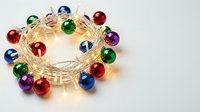 Colorful Christmas ornament string lights with multicolored baubles on white background for holiday decorations and festive seasonal celebrations.