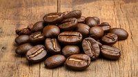 Fresh roasted coffee beans scattered on rustic wooden surface with natural lighting and detailed texture showing rich brown tones and distinctive bean shapes.