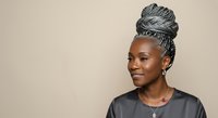 Young Black woman with gray braided updo hairstyle wearing dark casual shirt against neutral beige background, looking to side with confident expression for portrait and lifestyle use.