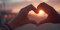 Hands forming heart shape silhouette against warm sunset sky with bokeh lights creating romantic atmosphere for love and connection concepts.