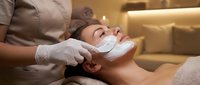 Young Asian woman receiving professional facial mask treatment at luxury spa with beautician applying white cream mask for skincare and relaxation.
