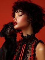 Asian woman with curly black hair wearing lace dress poses with small black dog against red background, dramatic fashion portrait with closed eyes and red lipstick.