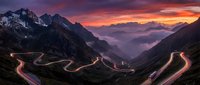 Dramatic mountain pass with winding road light trails at sunset. Snow-capped peaks and purple sky create stunning alpine landscape for travel and adventure concepts.