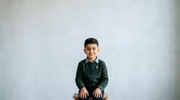 Young boy with dark hair and olive complexion, wearing a dark green long-sleeved shirt, smiling at camera against neutral white background. Suitable for family, education, and lifestyle design projects.