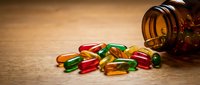 Colorful vitamin capsules and pills spilling from amber glass bottle onto wooden surface for health and wellness supplement concepts.