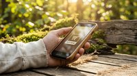 Hand holding smartphone with shopping cart buy now button outdoors on wooden surface in green nature setting for eco commerce concept.
