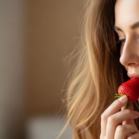 Young blonde woman enjoying fresh strawberry with closed eyes in soft natural light for healthy eating and wellness lifestyle concepts.