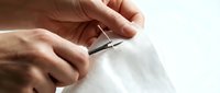 Hands carefully cutting white fabric with sharp scissors for sewing crafting tailoring project on bright surface for creative textile work.