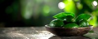 Fresh limes with green leaves in rustic wooden bowl against blurred natural background with bokeh lights, panoramic food composition.