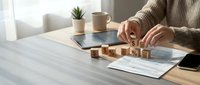 Woman arranging wooden blocks spelling PLAN on desk with tablet and documents in modern office workspace for business strategy and goal setting.