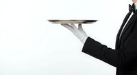 Professional waiter in formal attire holding silver serving tray with white gloves against clean background for hospitality and service industry concepts.