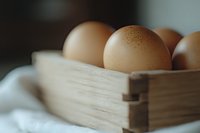 Fresh brown eggs in rustic wooden box on white linen cloth, shallow depth of field creates soft dreamy atmosphere for farm-to-table concept.