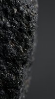 Dark volcanic rock with porous texture and metallic mineral inclusions on blurred background for geology education and natural science materials.