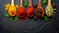 Colorful spices and herbs in wooden spoons on dark slate background. Turmeric, paprika, star anise, cardamom pods with fresh mint leaves for cooking.