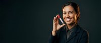 Professional businesswoman making phone call with smartphone, smiling confidently in dark suit against black background for corporate communication.