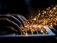 Hands typing on illuminated keyboard with magical golden light particles and sparkles emerging from keys, creating ethereal glow effect in dark background.