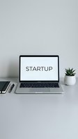 Laptop on a clean white desk displaying the word startup, with a small cactus plant, notebook, and pen, representing entrepreneurship and innovation.