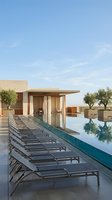 Modern luxury villa with infinity pool and lounge chairs on terrace under clear blue sky for vacation rental and hospitality marketing.