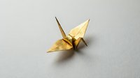 Golden origami crane on neutral background symbolizing peace, hope and traditional Japanese paper folding art for meditation and mindfulness concepts.