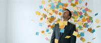 Happy businessman in suit celebrating success with colorful confetti falling around him against white background for business achievement concepts.