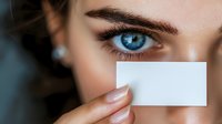 Close-up of woman with striking blue eyes holding blank business card, perfect for identity, branding, or contact information concepts.